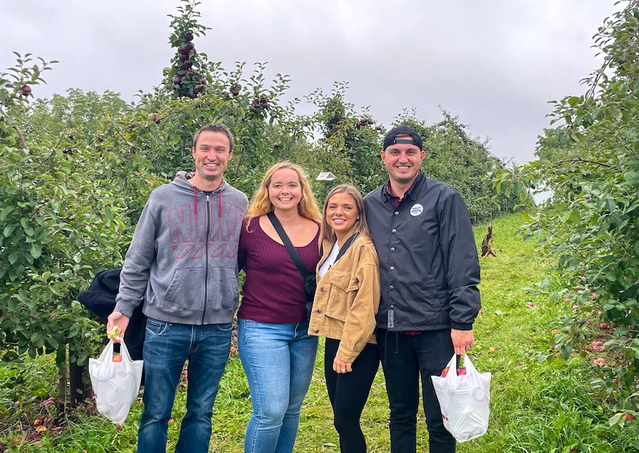 Fall Activities - two couples posing for a picture with their bags of apples among apple trees.