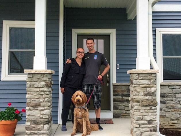 Couple posing in front of their front door with dog. 