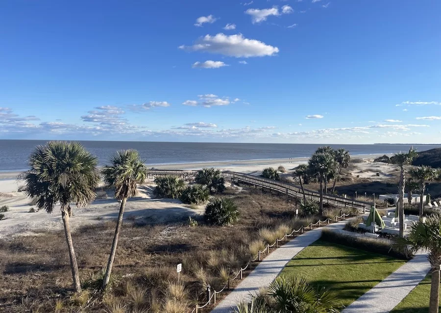 View of a oceanfront resort - Courtyard Jekyll Island - with walking path, palm trees, and sandy beach.