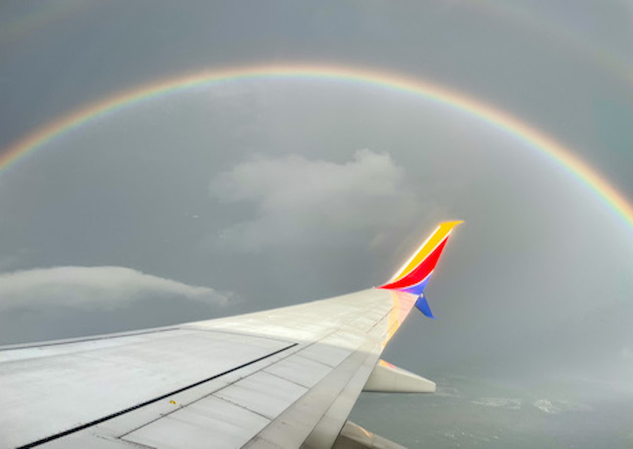 Southwest Airlines - Flight wing surrounded by rainbow in a gloomy sky.