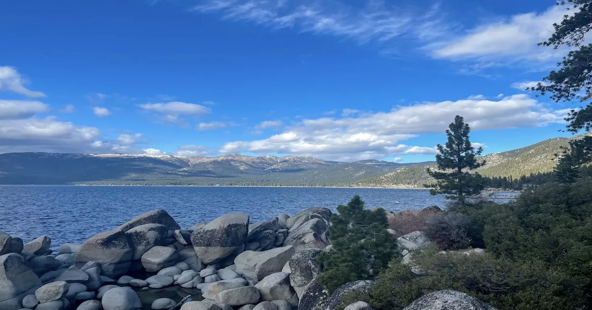 Lake Tahoe surrounding by mountains and pine trees and large rocks.