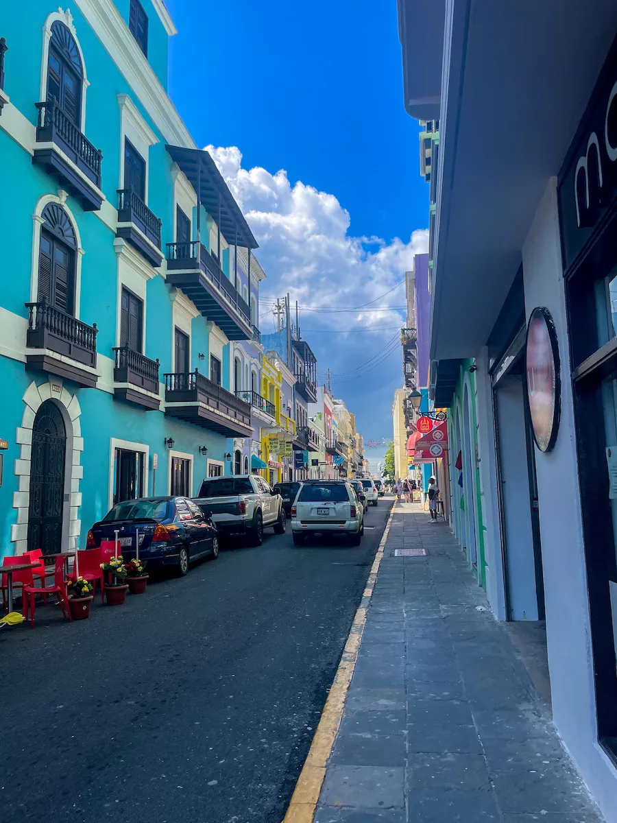 Street view of Old San Juan - street lined with cars, cloudy sky, and colorful buildings. 