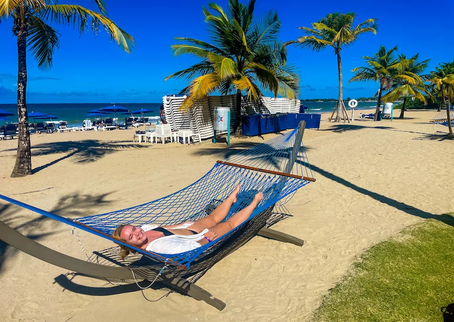Young woman in hammock on sandy beach surrounded by palm trees 