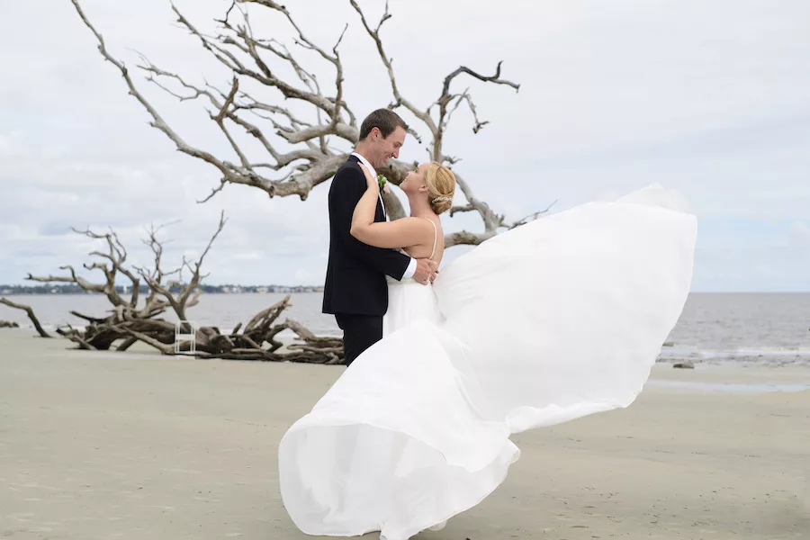 Husband and Wife taking wedding photos on beach in wedding attire with ocean in background. 