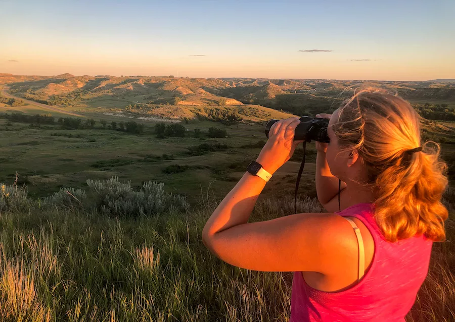 Lady looking through binoculars overlooking Theodore Roosevelt National Park as sun is setting