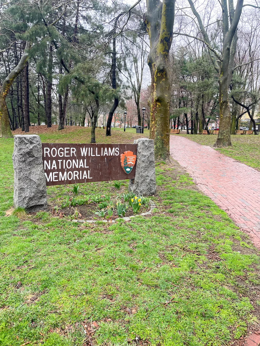 View of Roger Williams Memorial sign surrounded by path, trees and green grass 