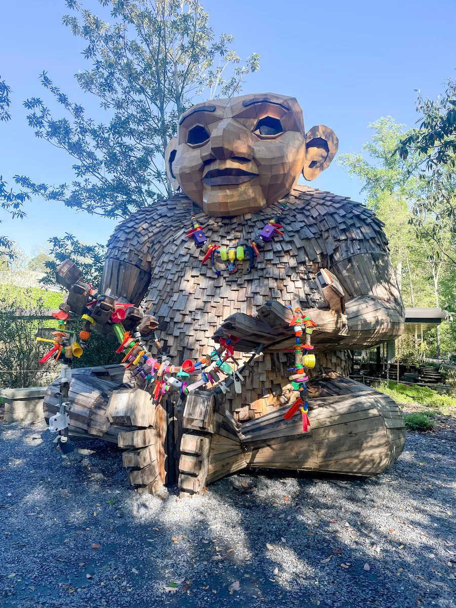 Sitting wooden troll holding a rope full of recycled materials. 