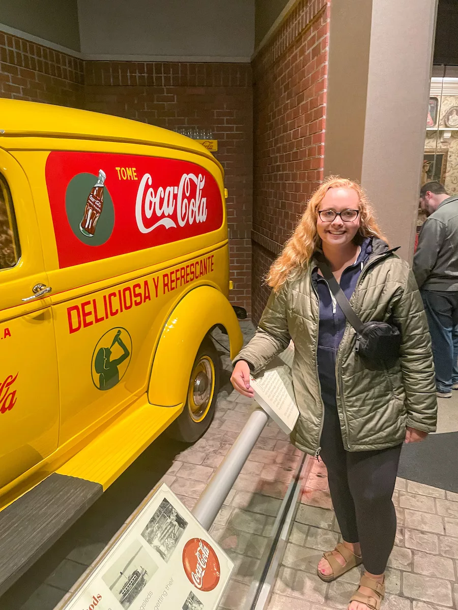 Bright yellow antique Coca-Cola truck with young woman standing next to it. 