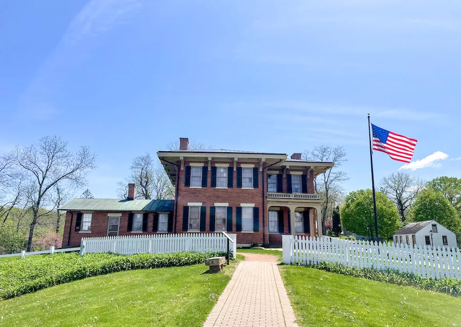 Charming brick house with a white picket fence. American flag on pole in front of house. 