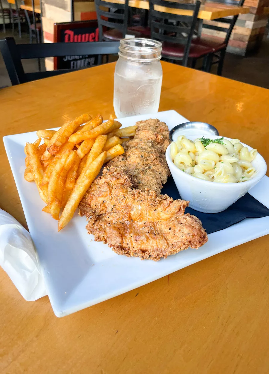 Image of chicken strips, fries, and mac and cheese with a glass of water. 