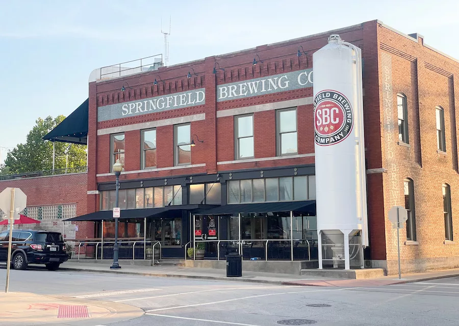 Restaurants in Springfield - Image of Springfield Brewing Co. from the outside (old brick building with outdoor seating). View of street and black car in view.