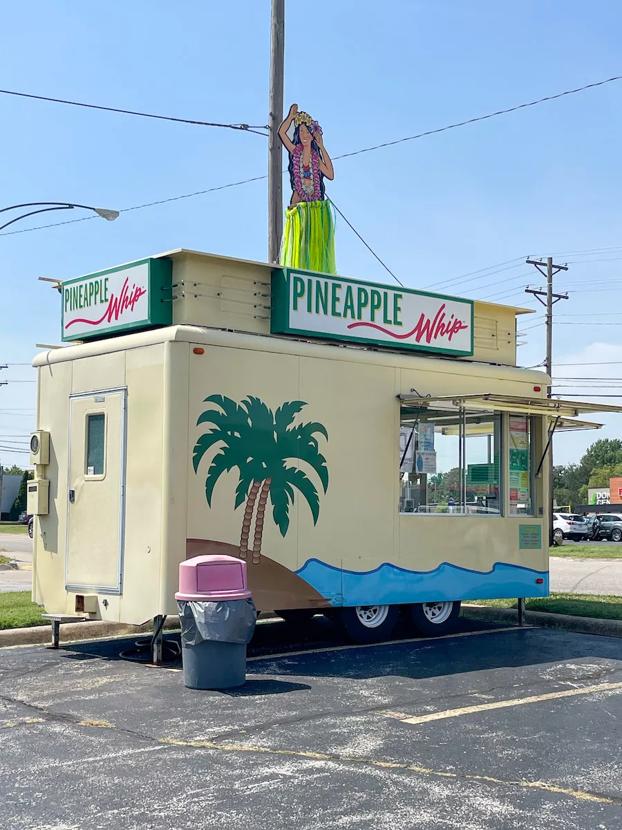 Food cart in a parking lot that is Hawaiian themed and serves Pineapple Whip. 