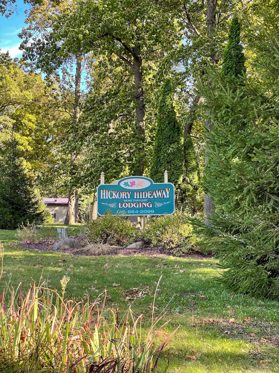 Entrance sign to Hickory Hideaway cabins surrounded by green grass, trees, and brush in Carroll County. 