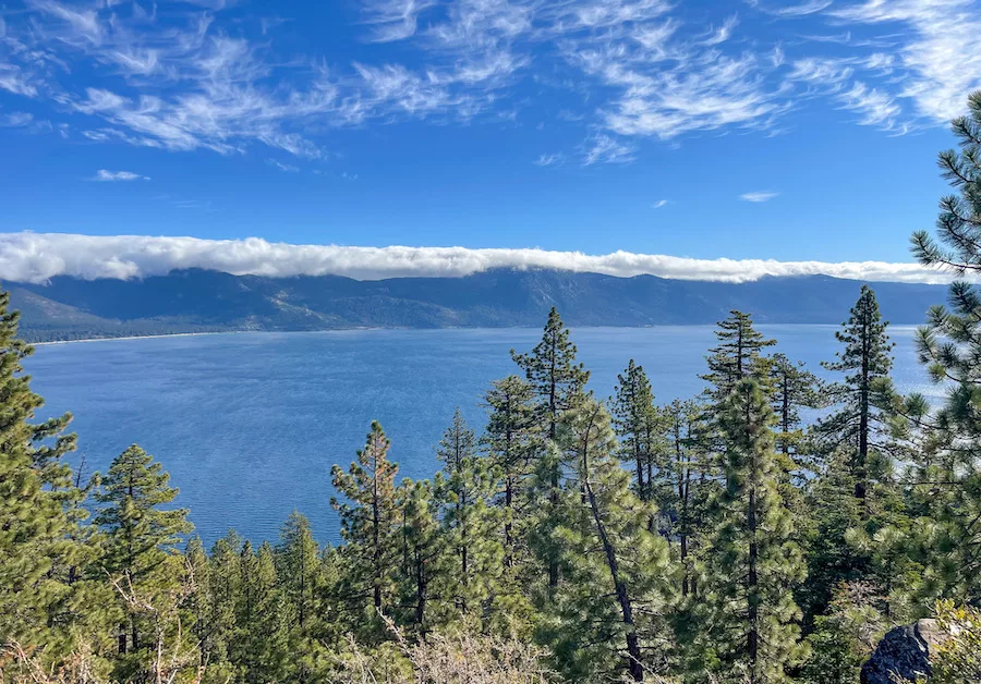 Image of Lake Tahoe surrounded by cloud-covered mountains on one side and evergreen trees on the other. 