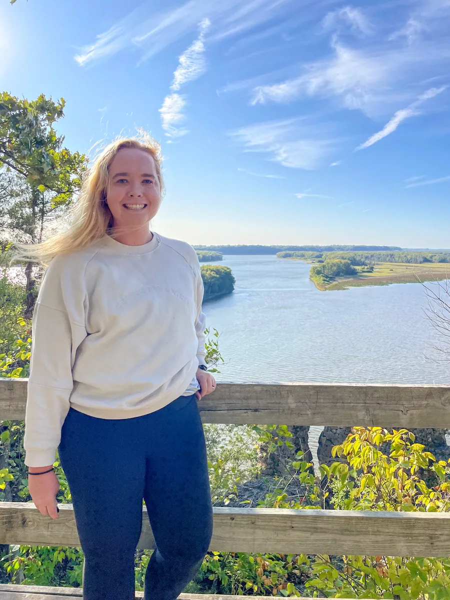 Young woman smiling at camera with Mississippi River surrounded by cloudy blue sky in background. 