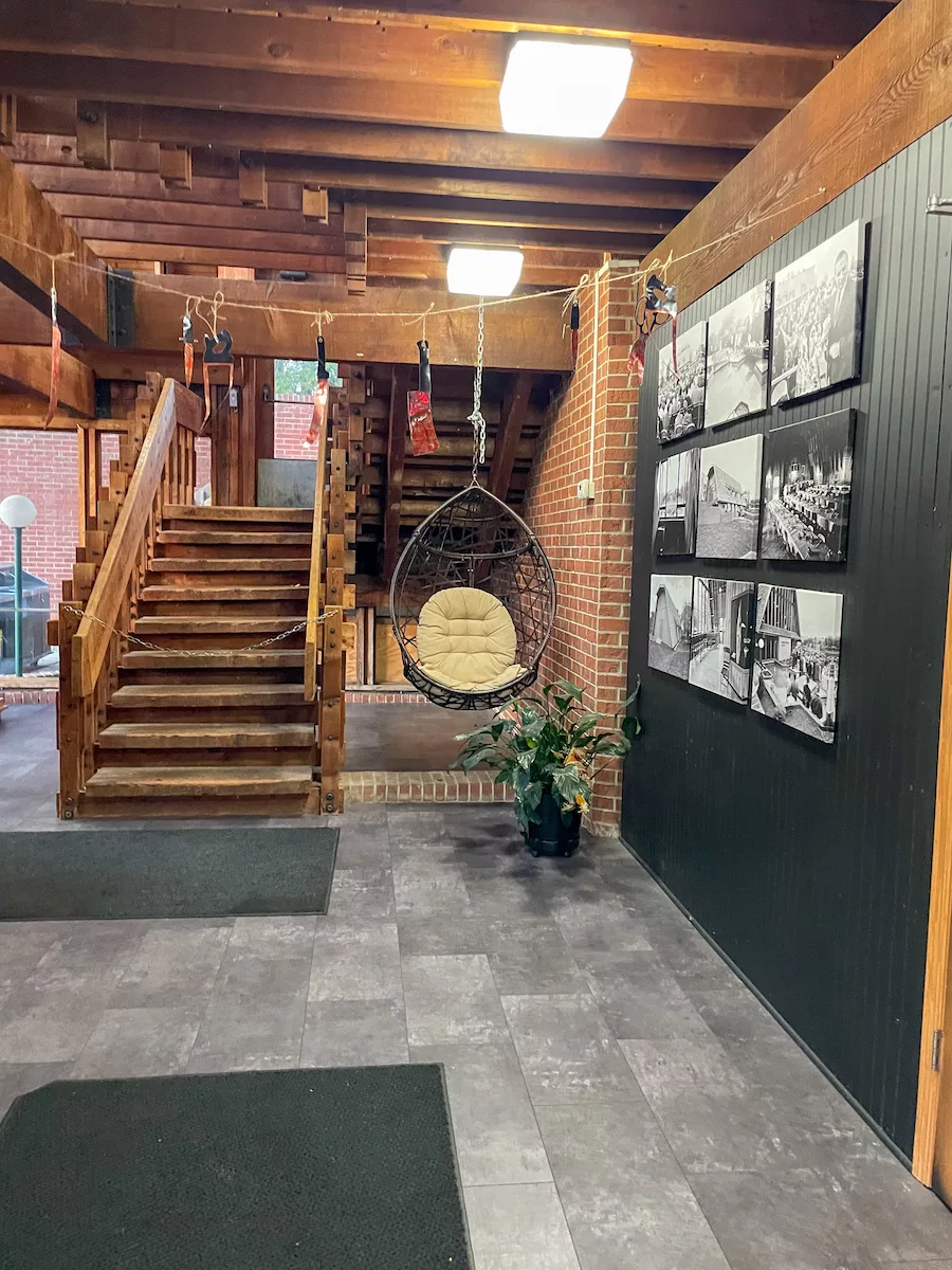 Inside view of The Copper Cow Entrance with stairs leading up, a swinging chair, and 9 black and white photos on the wall. 