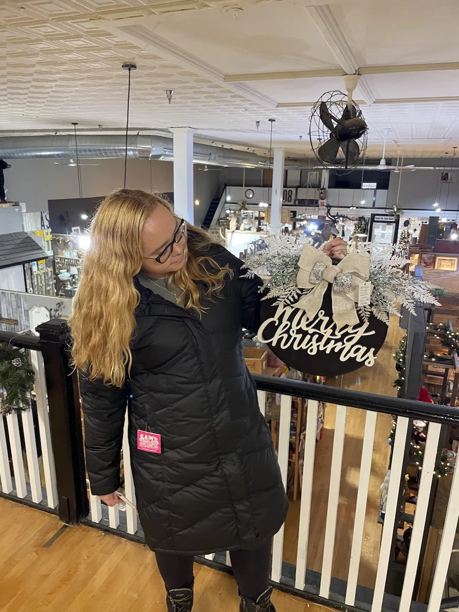 Woman holding Merry Christmas Door Sign in shop full of item - Things to Do in Janesville 