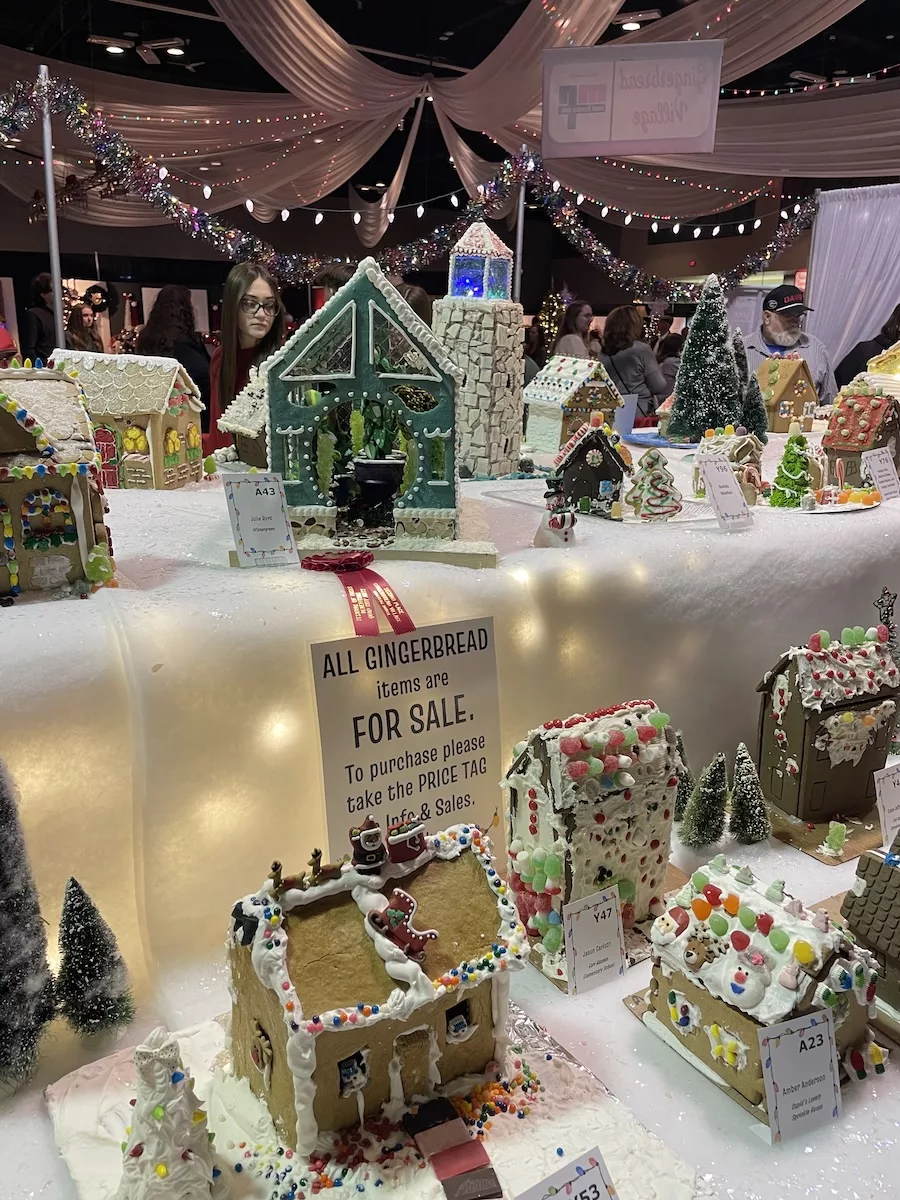 Row of decorated gingerbread houses at an event with people viewing the creations 