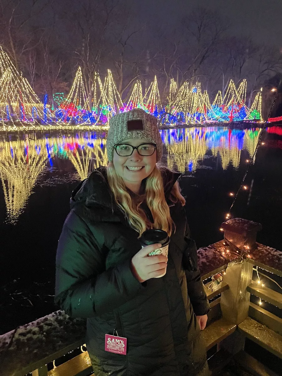 Young woman enjoying hot chocolate with holiday lights in background 