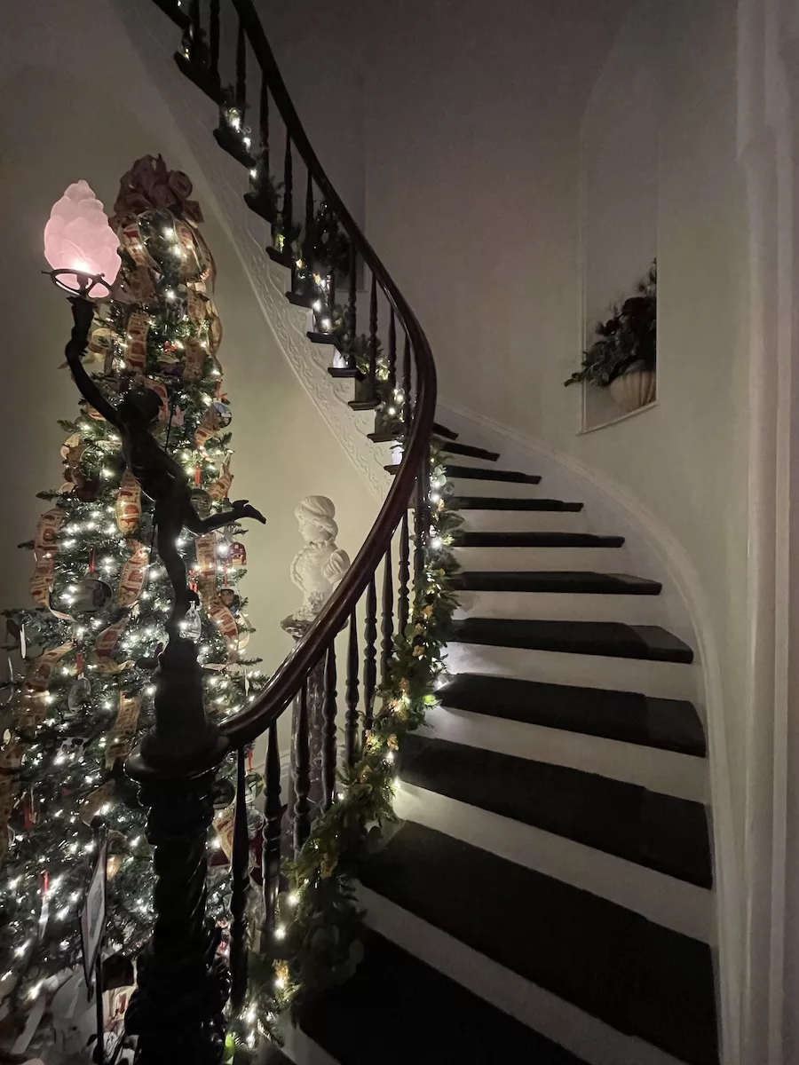 Curved wooden stairwell with garland, and decorated Christmas tree next to handrail 