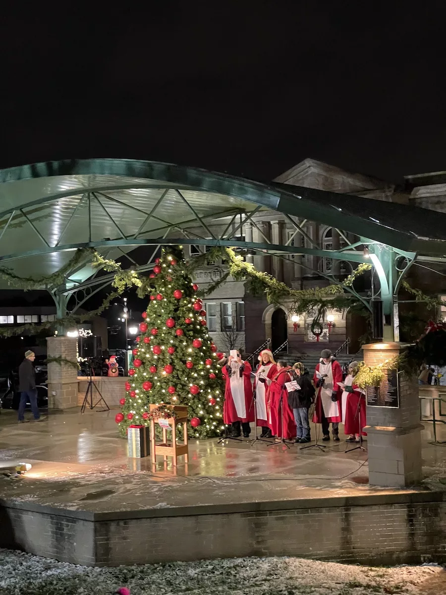 Large outdoor Christmas Tree surrounded by carolers at night. 