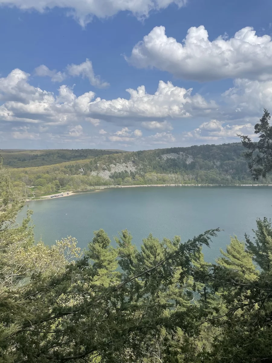 Image of blue lake surrounded by cloudy blue sky and green foliage - Devil's Lake Segment - Ice Age Trail
