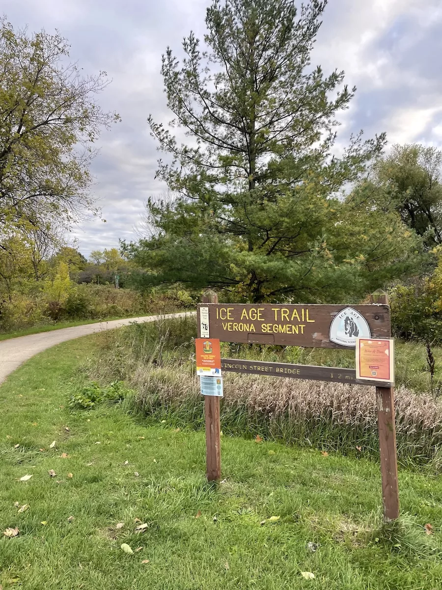Image of Ice Age Trail Sign for the Verona Segment surrounded by paved path, grass, and trees