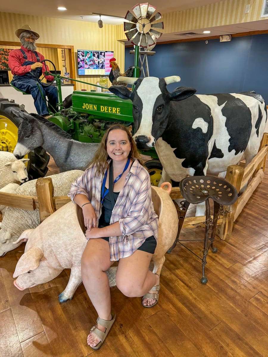 Image of young woman sitting on a sheep chair surrounded by plastic cow and farm set-up at Blue Gate Garden Inn