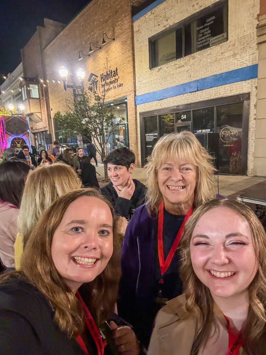 Group of three women smiling for a photo while standing outside at night. 