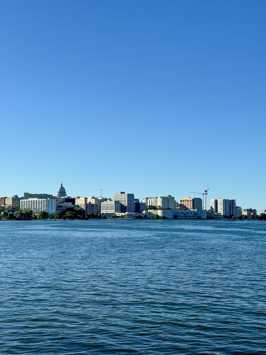 Image of the Madison, Wisconsin skyline with Lake Monona in front of it and a clear blue sky. 