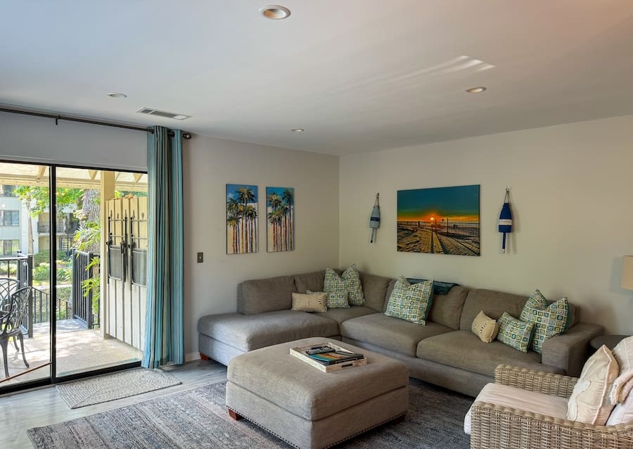 Image of a put-together living room in Hilton Head Island with a couch and chair, paintings, and sliding glass door leading to a balcony. 