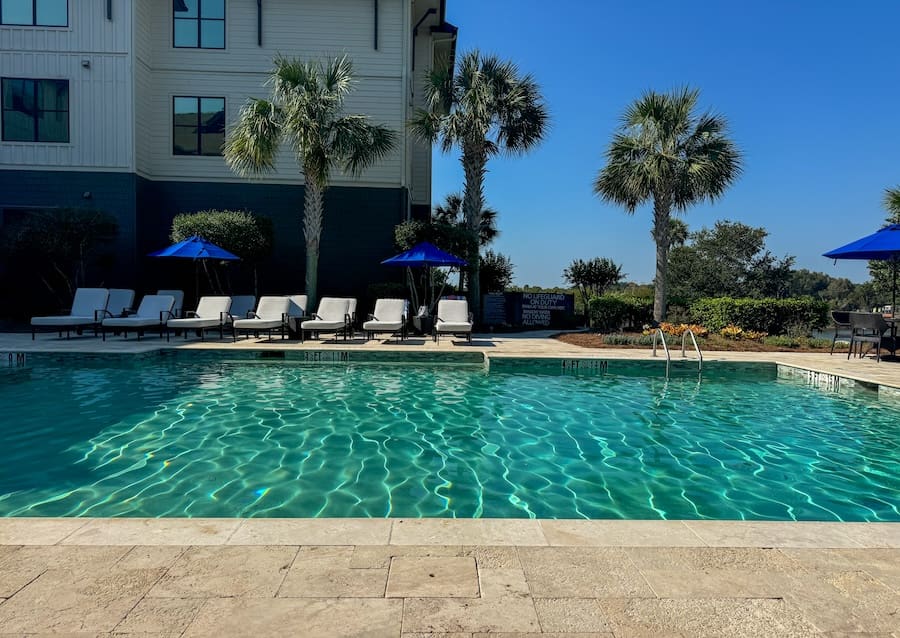 Image of pool with turquoise water, sun loungers, and palm trees surrounded by a hotel building - Charleston Kiawah Island/Andell Inn