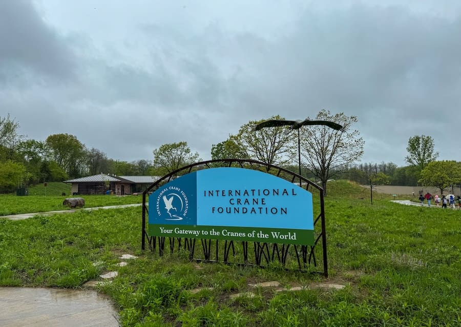 Image of an entrance sign to the International Crane Foundation surrounded by a grassy lawn and a cloudy gray sky.