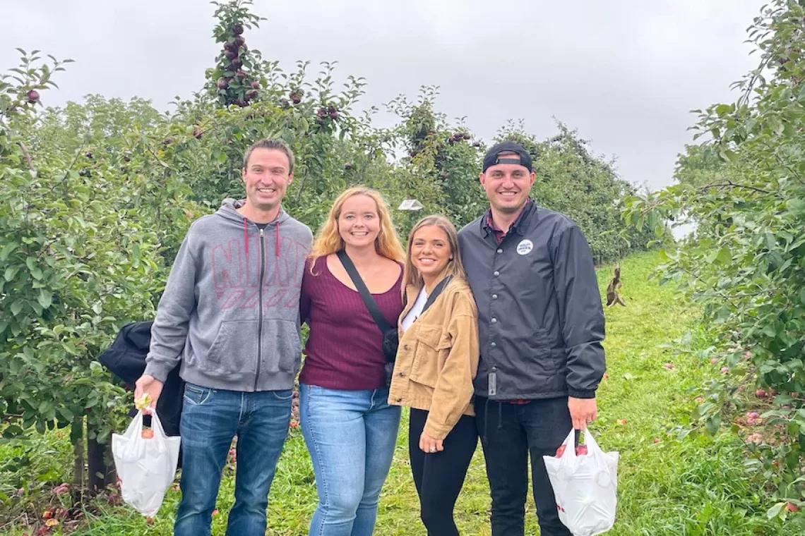 Two couples posing for a photo with two bags of apples in an apple orchard after apple picking