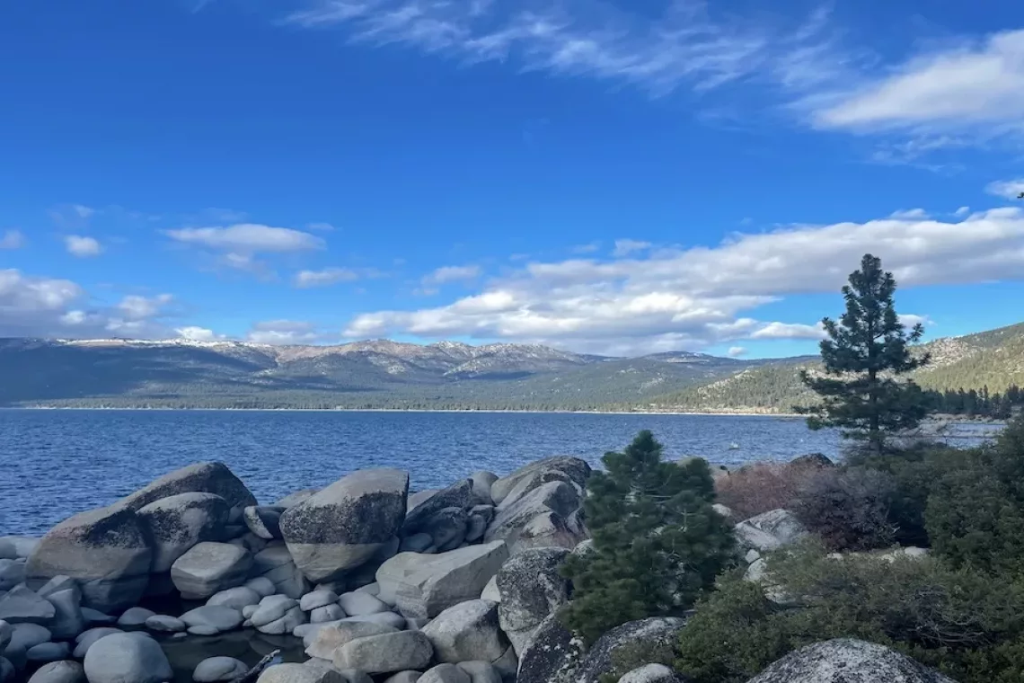 Lake Tahoe surrounding by mountains and pine trees and large rocks.