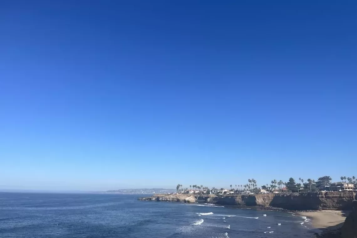 View of Ocean Beach San Diego from OB Pier featuring blue ocean and blue sky and city in the background.