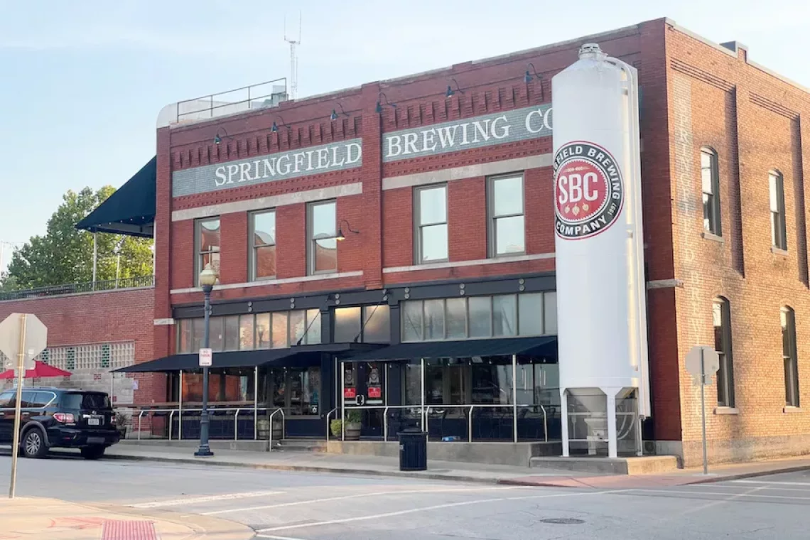 Restaurants in Springfield - Image of Springfield Brewing Co. from the outside (old brick building with outdoor seating). View of street and black car in view.