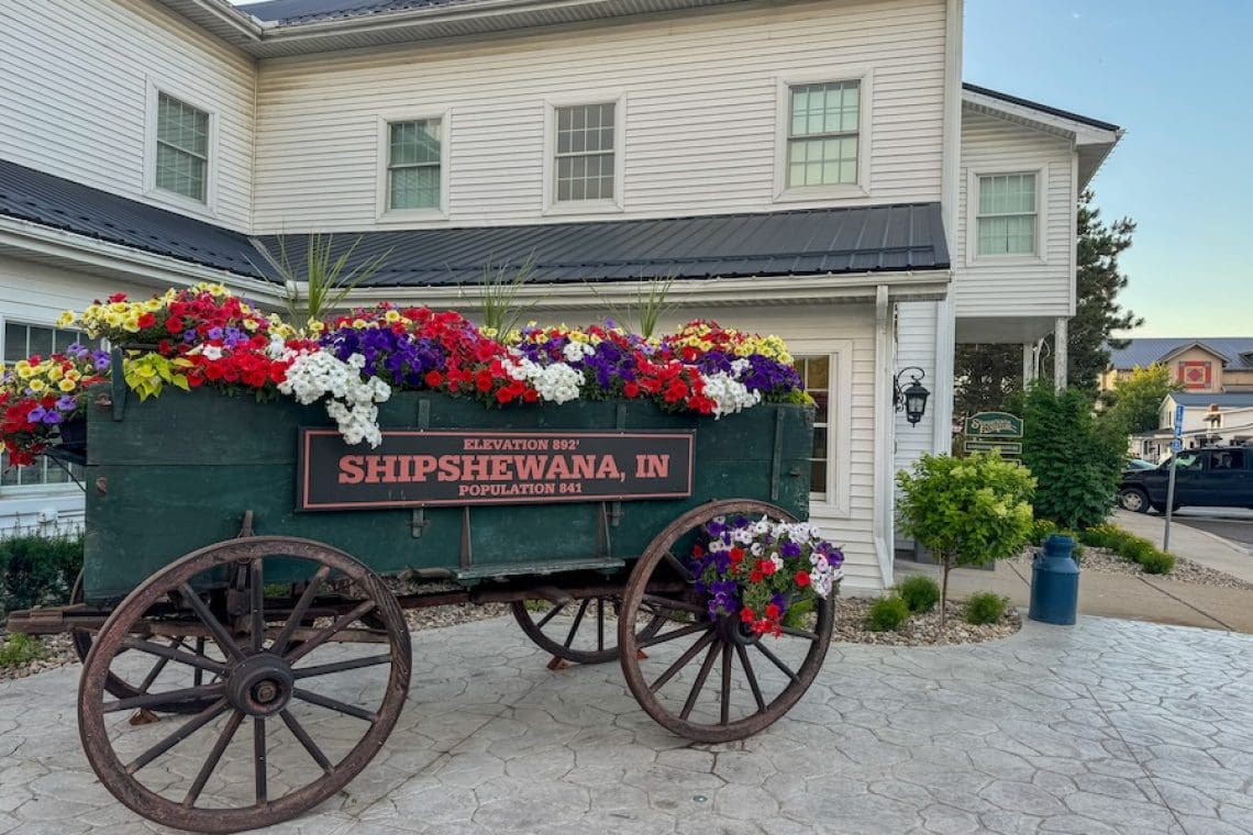 Image of buggy filled with colorful flowers and Shipshewana plaque with population sign - Guide to Shipshewana